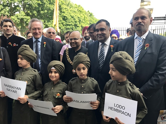 Children dressed as Labour Corps holding up names of those who served the British during World War I. High Commissioner Y K Sinha (2nd from Right) looks on.